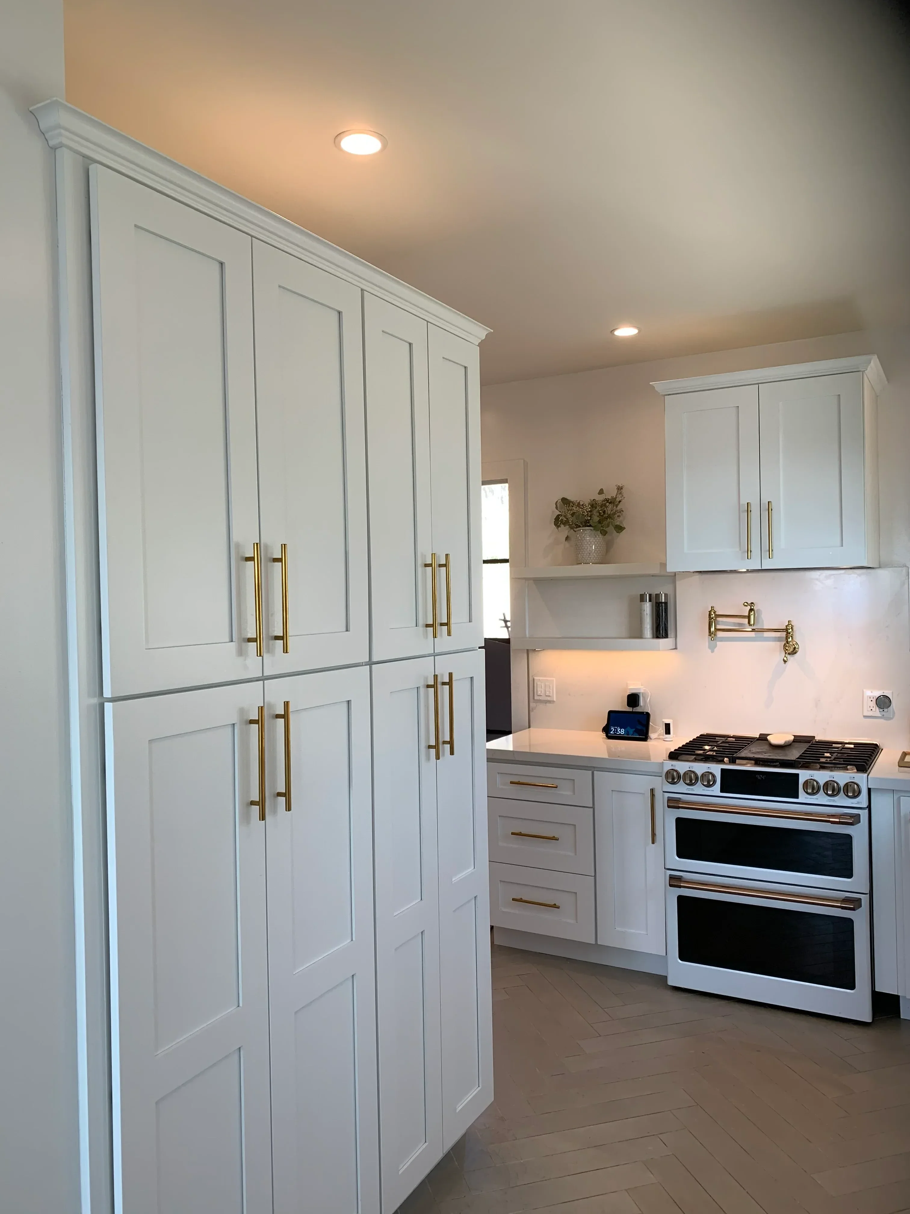 White kitchen cabinets with brass handles, recessed lighting, and stainless steel appliances