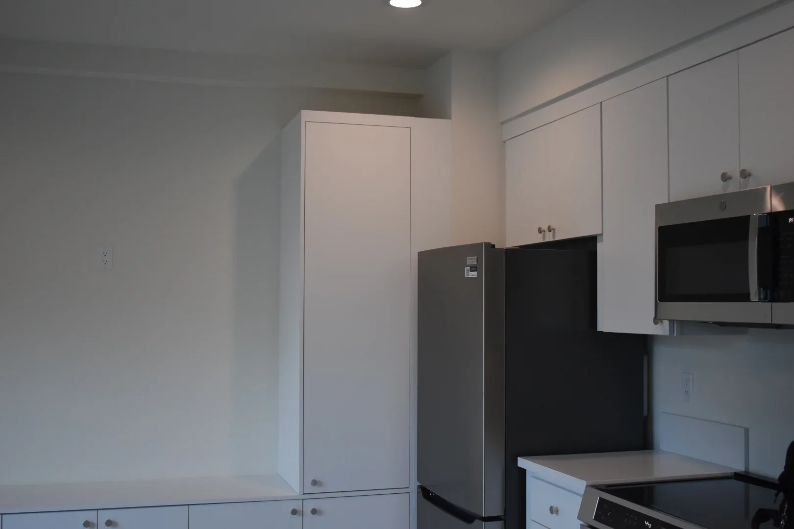 White kitchen cabinets with stainless steel refrigerator, microwave, and cooktop installation