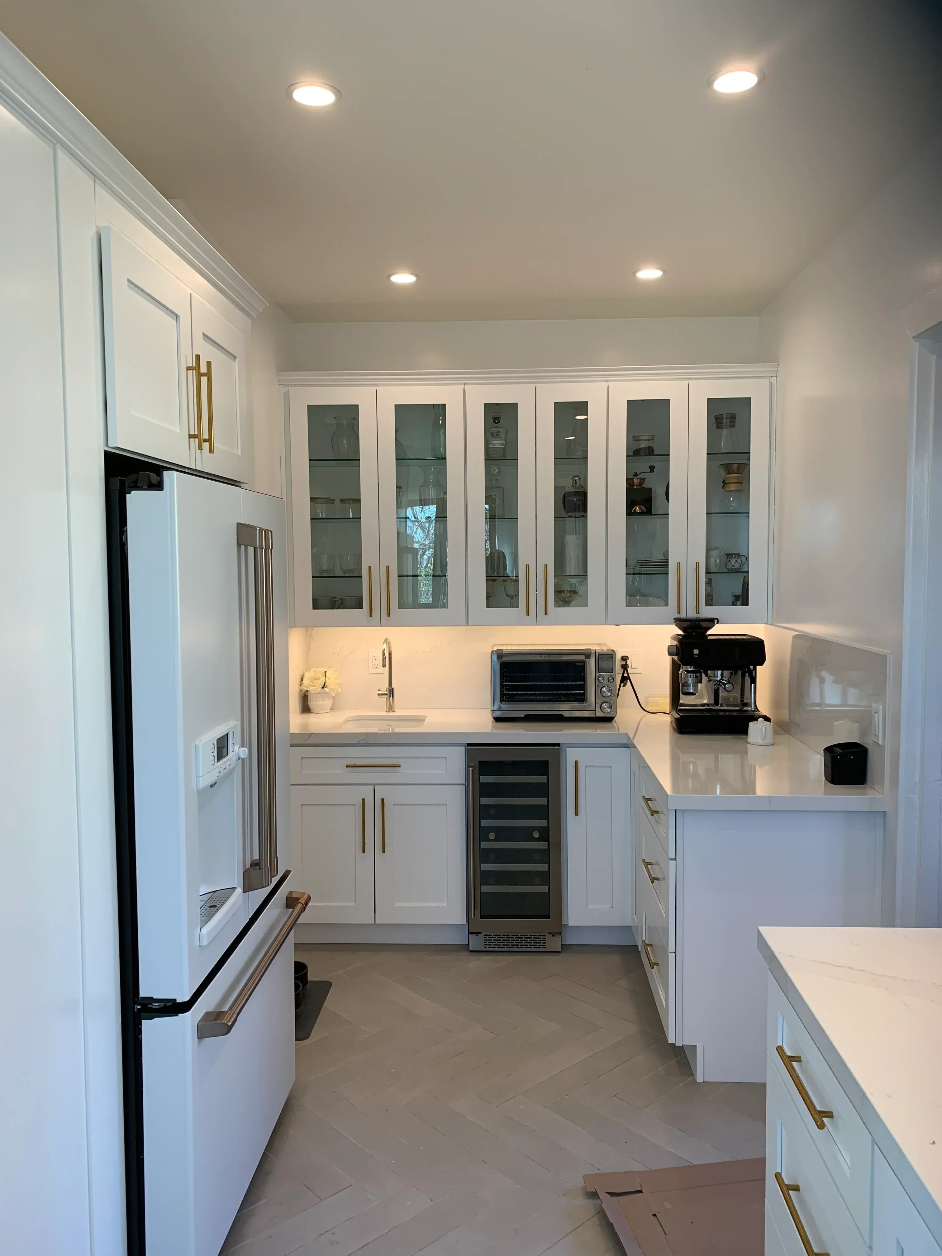 White kitchen cabinets with glass doors, recessed lighting, brass hardware, and electrical installation in progress