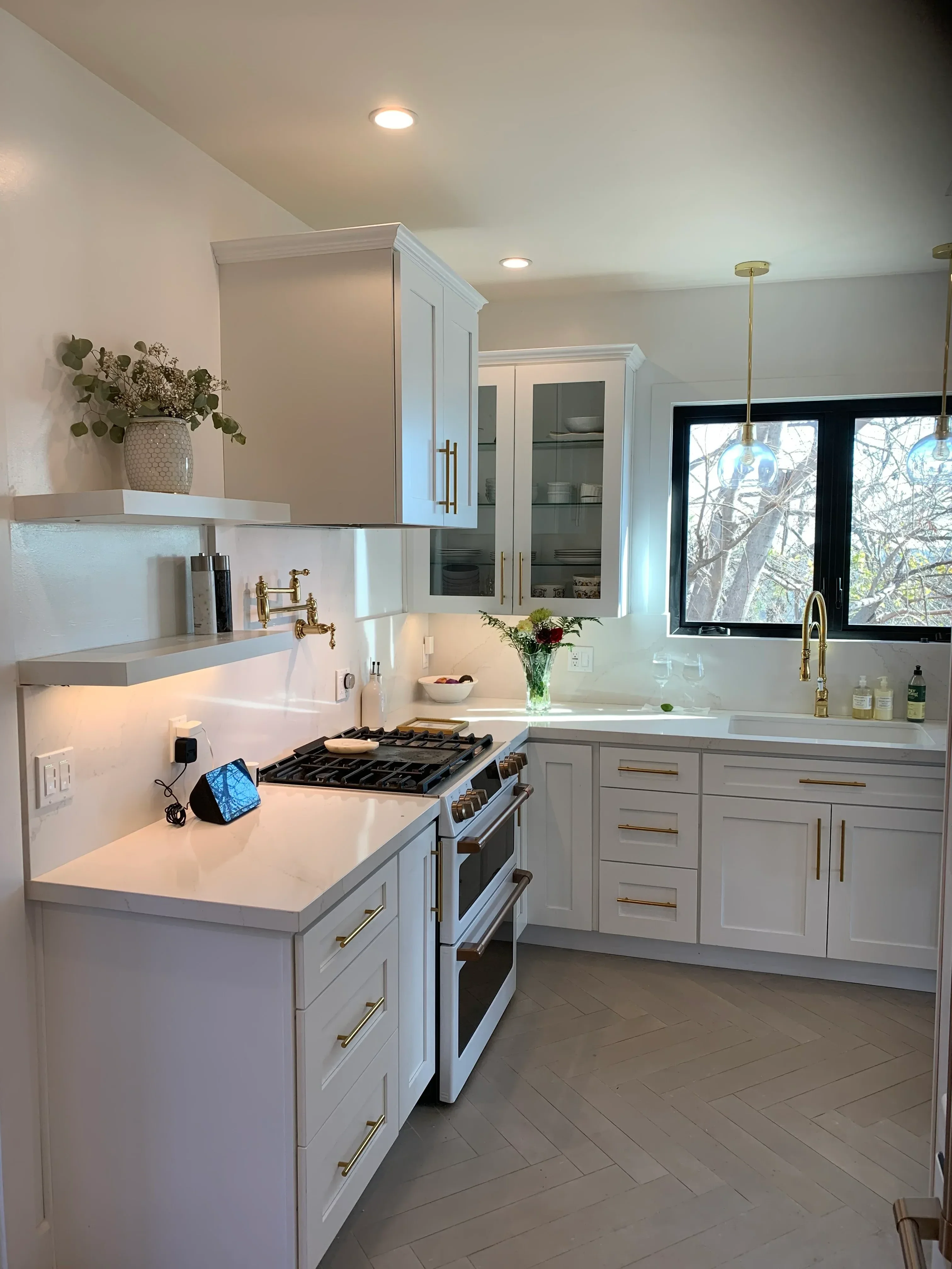 White kitchen cabinetry with brass pulls, black range hood, and bathroom vanities with vessel sinks