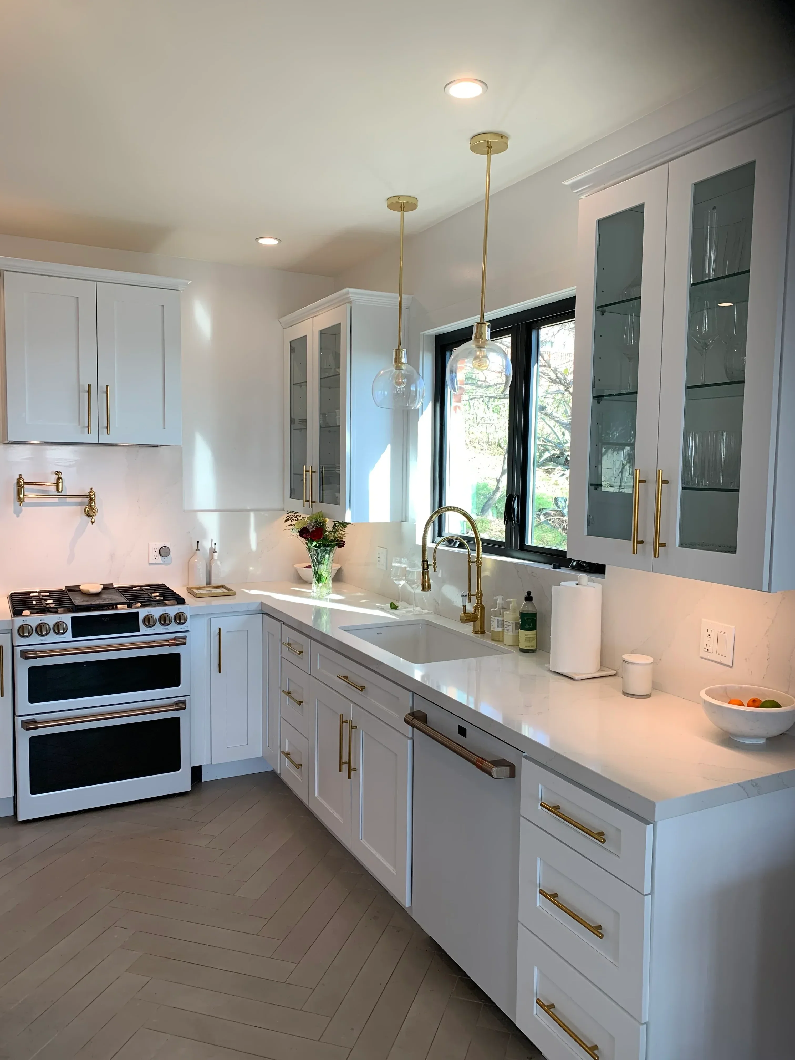 Modern kitchen with white cabinetry, brass fixtures, stainless steel appliances, and skylight windows