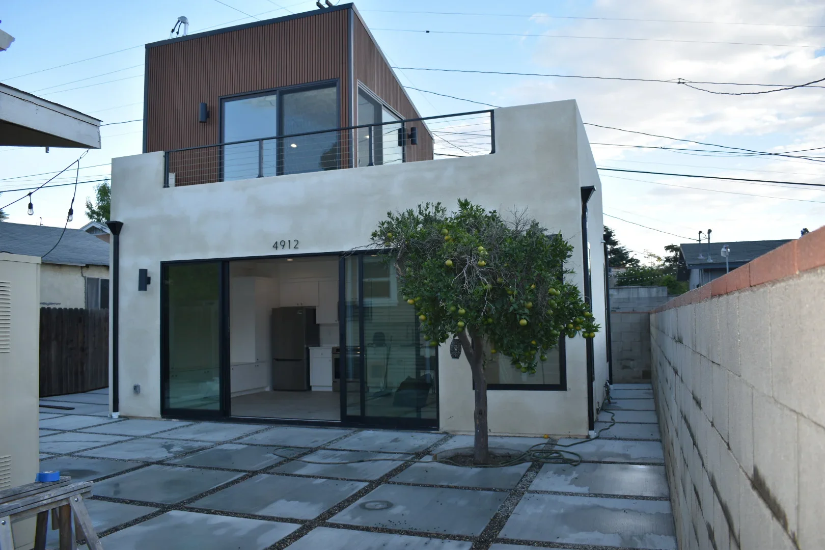 Modern home addition with corrugated metal upper level, white stucco, black-framed windows, and concrete paver patio