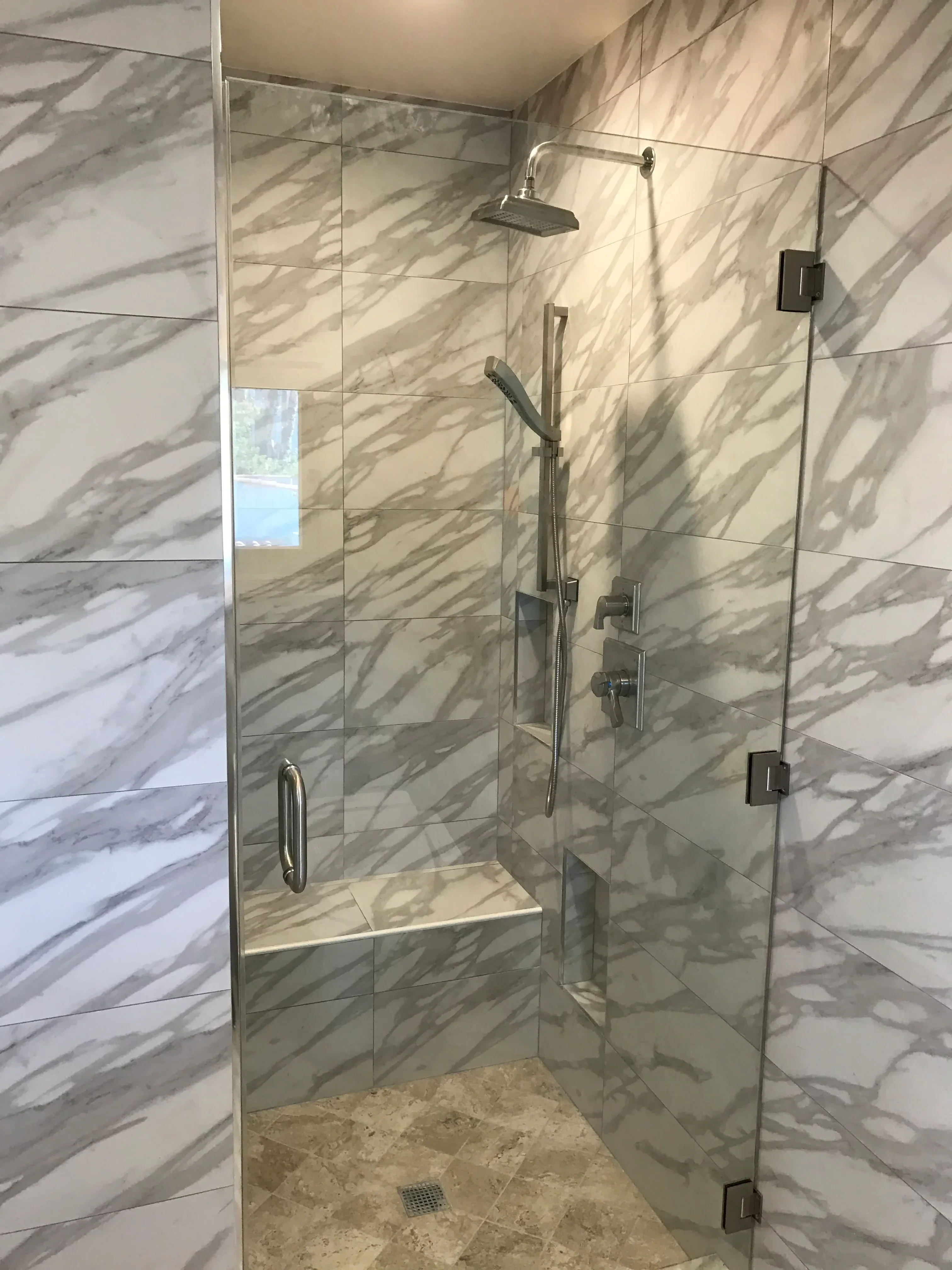 Marble tile shower with frameless glass door and brushed nickel fixtures