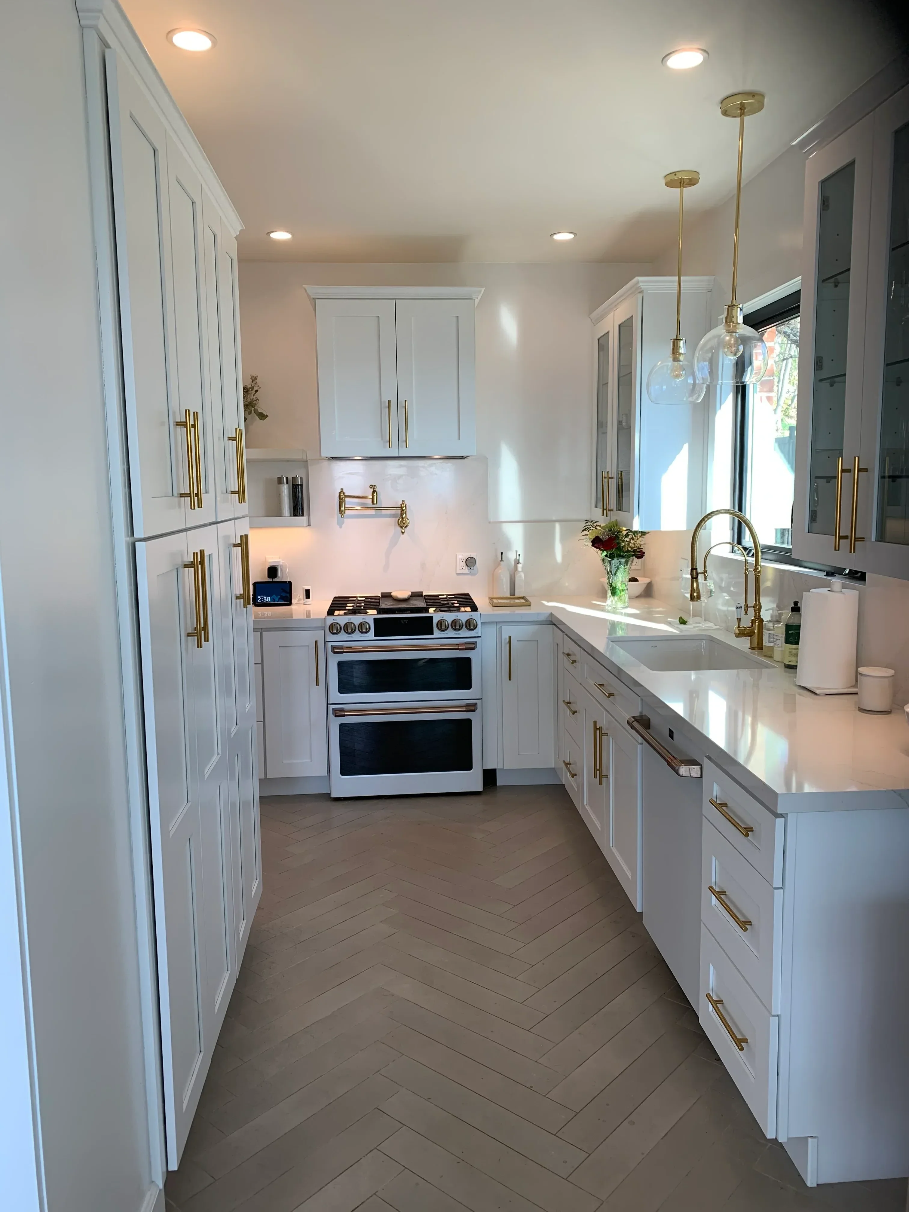 Modern kitchen with white cabinetry, brass hardware, herringbone backsplash, and dual wall ovens
